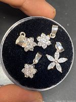 Four sterling silver flower-shaped charms with clear crystals displayed on black velvet.