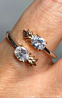 Close-up photo of sterling silver crossover ring with two oval clear crystals and leaf-like accents worn on finger.