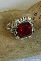Close-up of sterling silver ring with large red gem and clear crystal accents on a wood surface.