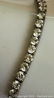 Close-up of tennis bracelet showing round clear crystals and tarnished silver metal.