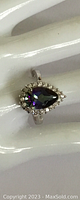 Front view of a sterling silver ring featuring a pear-shaped multicolor gem surrounded by small clear crystals on a white display hand.