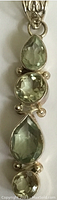 Close up of faceted green gemstones in pear and oval shapes set in sterling silver pendant.