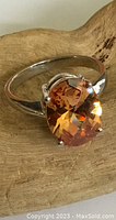 Close-up image of the sterling silver ring showing the large faceted orange gemstone and prong setting.