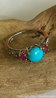 Close-up front view of ring showing central turquoise-colored cabochon and flanking pink-colored stones