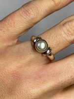 Close-up of sterling silver ring with a single genuine pearl shown worn on a finger, highlighting the pearl and silver band details.