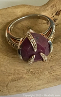 Sterling silver and ruby claw ring on wooden display, showing stone and prongs detail.