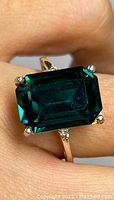 Close-up of the sterling silver ring featuring a large rectangular emerald cut green stone with four prong setting, shown being worn on a finger.