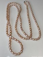 Full view of the full length pink pearl necklace arranged on a flat surface to show length and bead size