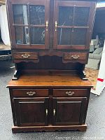 Photo of wooden china hutch with glass doors, showing front view with brass handles and wood finish.