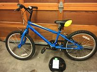 Blue 20-inch Charge Supercycle kid's bike with knobby tires and black and yellow stadium style seat, parked inside garage.