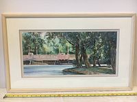 Full view of framed watercolor painting showing a bridge over water with trees on the right side, framed in light wood with white matting.