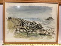 Frontal image of the original watercolor painting showing the coastal landscape with rocks, ocean, and sky, framed in a wooden floating frame with glass.