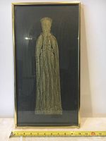 Full view of framed brass rubbing showing entire figure with ruler at base for size reference.