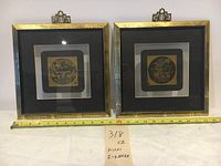 Two framed Chinese etchings with a measuring tape laid out in front showing 11 inches in width. Both frames are square with gold trim and black mats.