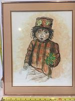 Framed watercolor painting featuring a child in a striped jacket and decorated hat holding flowers, with signature visible.
