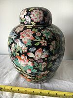 Full view of vintage Chinese porcelain jar with colorful floral patterns and fitted lid, measuring around 10.5 inches tall and 8 inches diameter as shown with tape measure.