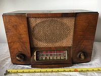 Front view showing wooden cabinet, fabric speaker cover, tuning dial with frequency scale, and two knobs.