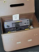Kodak Carousel 4600 slide projector placed inside its original brown carrying case with two remote controls and instructions visible, showing the condition and contents of the lot.