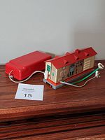 Front and side view of vintage metal toy train station with attached battery pack and wires on wooden surface.