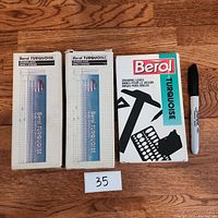 Top-down photo showing all three packages of Berol Turquoise drawing leads lying flat on a wood floor alongside a Sharpie marker for scale.