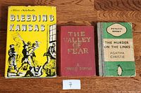 Three books displayed side by side on wooden surface: 'Bleeding Kansas', 'The Valley of Fear', and 'The Murder on the Links'.