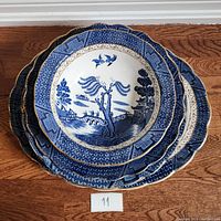Three stacked blue and white porcelain plates with willow pattern and scalloped edges on a wooden surface.