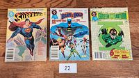 Lot of three DC Comics on wood surface, showing full front cover of each comic: Superman, The Brave and the Bold, Green Lantern