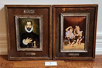 Pair of framed enamel on copper prints, one portrait of a man and one of two children, side by side on floor.