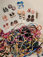 Overview photo of polymer clay earrings arranged in pairs above a large pile of mixed beaded lanyards and bracelets
