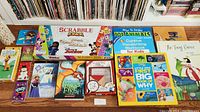 Photo shows the full assortment laid out including Scrabble Junior box, multiple kids books including Wings of Fire, The Frog Prince, How to Draw 101 Animals, and other educational material.