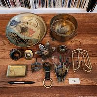 Overview of all 11 items arranged on wooden surface showing variety of metal objects including painted decorative piece, container, and trinkets.
