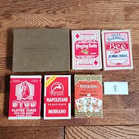 Overview photo of all 6 playing card decks and the American Playing Card Company box on a wooden surface with a number 8 placard