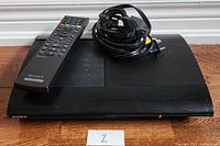 Sony PlayStation 3 Slim console with remote and cables on top, showing front and part of top surface.