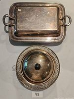 Top view of the rectangular silver plated serving tray and the covered round silver plated dish with base and black knob lid.