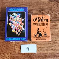 Set of two card decks side by side on wooden surface labeled with number 4, namely the Tree of Life Tarot and Gypsy Witch Fortune Telling playing cards.