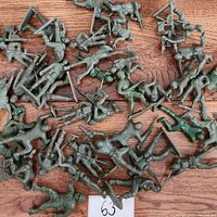 Overhead view of multiple green plastic Tim Mee toy soldiers in various poses on a wooden surface.