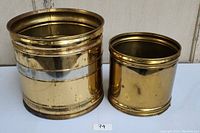 Two brass vases of different sizes with tarnished areas visible on reflective surfaces.