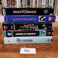 Five VHS tapes stacked, showing spines with titles: Prince of Darkness, The Vampire Lovers, Plan 9 from Outer Space, Horror of Dracula, The Andy Kaufman.