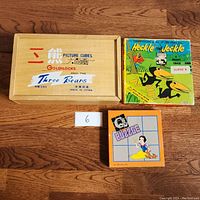 Top view of all three items on wooden floor: Goldilocks picture cubes box, Heckle and Jeckle movie cassette, and Snow White puzzle box.