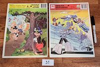 Both vintage frame tray puzzles side by side on wooden floor, with marker for scale.