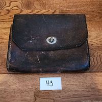 Front view of a vintage brown leather satchel placed on a wooden surface with a label marked 43 below it.
