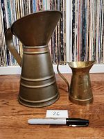 Two vintage water jugs side by side on wooden floor with vinyl records in the background, showing size difference and condition.