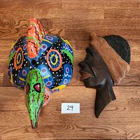 Photo showing colorful Guatemalan chicken mask next to carved wooden woman's face art on wooden floor.