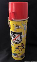Full view of vintage thermos showing yellow body with sport illustrations and red lid