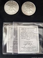 Two coin obverses and two authentication certificate cards in protective flips displayed on black background