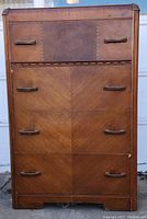 Full front view of the Art Deco 4 drawer waterfall dresser showing veneer front with chevron and solid panel design, wood handles, and visible chip on bottom drawer right corner.