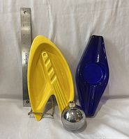 Yellow ceramic ashtray and blue glass diamond-shaped ashtray with round chrome lighter in front, ruler for scale included.