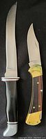 Two Buck cutting tools together on dark background, showing fixed blade with black handle and folding knife with wood and brass handle