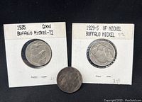 Three Buffalo nickels displayed with two mounted in collectible holders labeled '1935 Good Buffalo Nickel T2' and '1929-S VF Nickel Buffalo Nickel T2', with a third heavily worn coin loose in front of them.