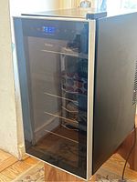 Overall view of the closed Haier beverage refrigerator with glass door and visible metal racks inside